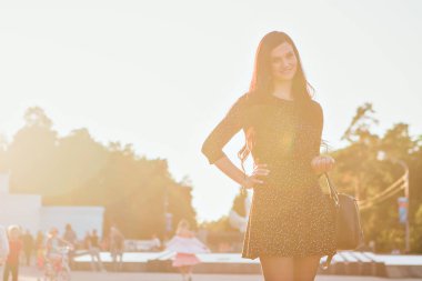 ışık sokakta yürürken bir çanta ile siyah bir elbise güzel esmer. Kadın aksesuarları, kozmetik, makyaj reklamını