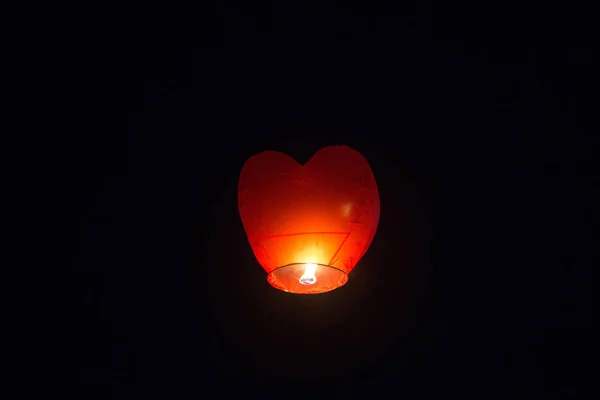 Red Chinese heart-shaped flashlight flies in the night sky. Happy birthday summer and wedding concept. Isolated on black background — стокове фото