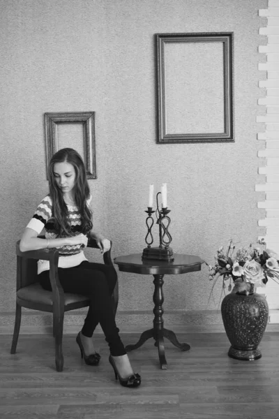 A menina está sentada em uma mesa com velas, ao lado de um vaso de flores e molduras vazias. Conceito de decoração de interiores, design — Fotografia de Stock