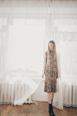 Makyajsız güzel bir kız perdenin arkasından dışarı bakar, pencerede bir kadın. Reklam doğal makyaj kavramı, sabah eğlence