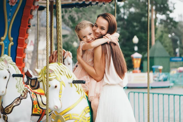 En liten flicka med sin mamma som rider i parken på en leksaks häst på karusellen. Underhållnings branschkoncept, familjedag, barn parker, lekplatser — Stockfoto