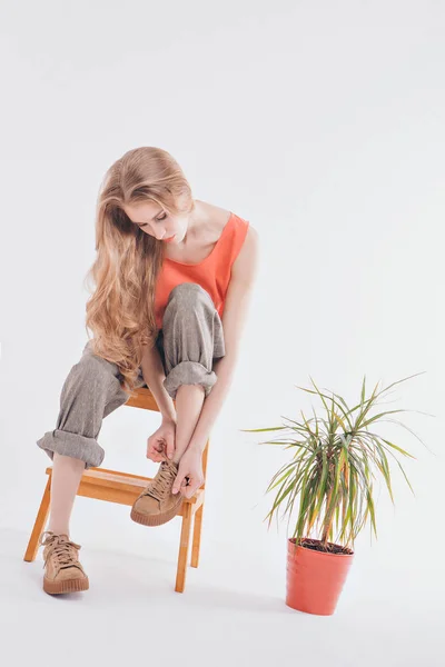 advertising clothes: girl wears shoes on a white background. model sitting on a chair, next to a flower in a pot.