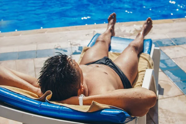 O conceito de um dia de descanso, relaxamento, reflexão, banhos de sol, bronzeado o homem bronzeado repousa sentado em uma cadeira perto da piscina. Expressão calma do rosto, postura relaxada — Fotografia de Stock