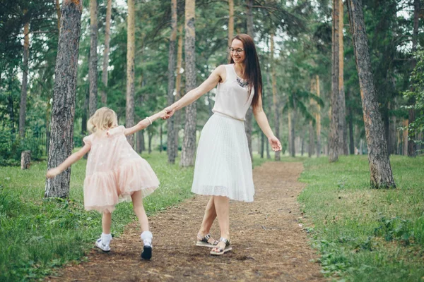 Begreppet Walking, hälsosam livsstil. En kvinna och en flicka som går hand i hand i skogen. Mamma och dotter i vita klänningar — Stockfoto