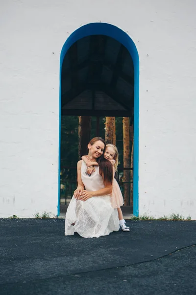 Matka a dcera u bílé zdi. žena a holčička se dívají ven z oblouku — Stock fotografie