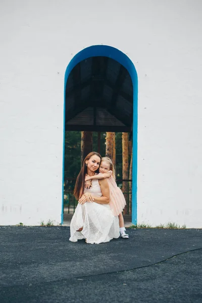 Мати і дочка біля білої стіни. жінка і маленька дівчинка виглядають з арки — стокове фото