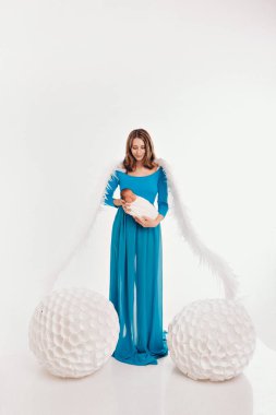 Mavi elbiseli, melek kanatlı, beyaz arka planda yeni doğmuş bir bebeği tutan bir kız. Bir melek kadın ve çocuğun büyük beyaz topları vardır. Noel konsepti, mistik yaratıklar, Cadılar Bayramı