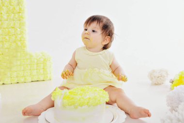 Küçük bir kız pastayı elleriyle şöminenin arka planında yer. Bebek yiyecekle kaplıydı. doğum günü partisi