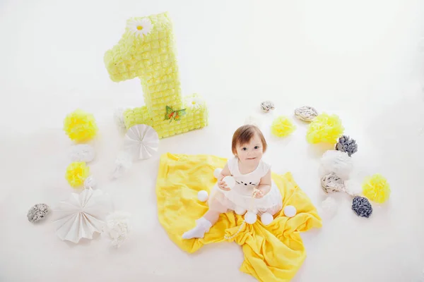Verjaardagsfeest: meisje zit op de vloer tussen de decoratie: nummers 1, kunstbloemen en witte ballen — Stockfoto