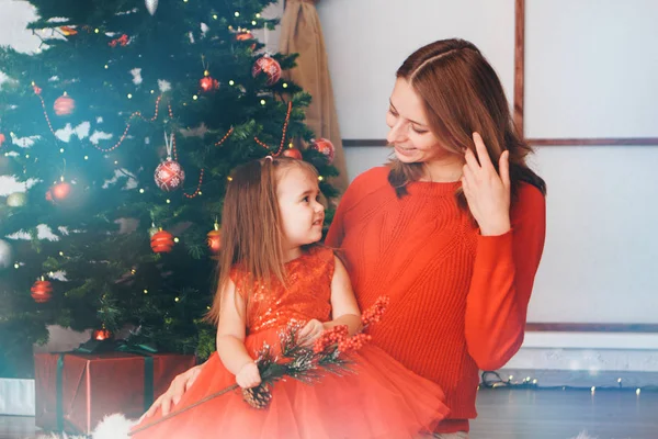 Мать и дочь в красной одежде разворачивают новогодние подарки под елкой. концепция празднования Рождественской полуночи — стоковое фото