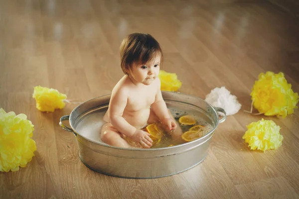 Een klein meisje baadt in een bad met citroen en grapefruit. Een kind wast zich in een bassin tussen gele bloemen. concept van kindertijd, gezondheidszorg, Ivf, hygiëne, citrustherapie — Stockfoto