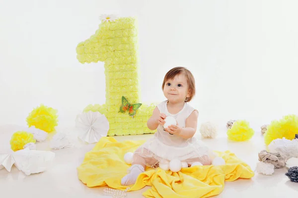 Celebração de aniversário: menina sentada no chão entre a decoração: números 1, flores artificiais e bolas brancas — Fotografia de Stock