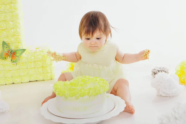 Uma menina come bolo com as mãos no chão da lareira. O bebé estava coberto de comida. festa de aniversário — Fotografia de Stock