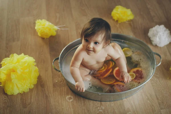 Een klein meisje baadt in een bad met citroen en grapefruit. Een kind wast zich in een bassin tussen gele bloemen. concept van kindertijd, gezondheidszorg, Ivf, hygiëne, citrustherapie — Stockfoto