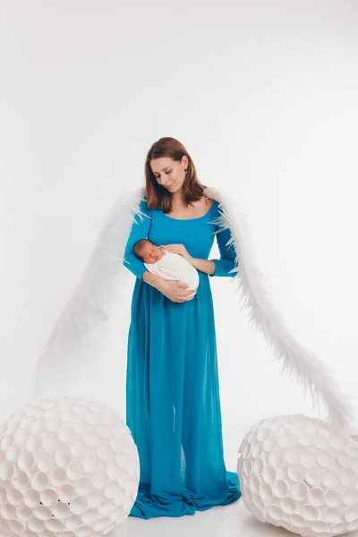 Une fille en robe bleue avec des ailes d'ange tenant un nouveau-né sur un fond blanc. Un ange-femme et un enfant ont de grosses boules blanches. Le concept de Noël, créatures mystiques, Halloween — Photo