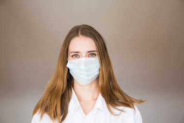 Bej arka planda tıbbi maske takan bir kadının portresi. Tıbbi ekipmanların tanıtımı.