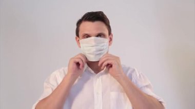 Beyaz arka planda tıbbi maske takan bir adamın portresi. Tıbbi ekipmanların tanıtımı. Adam işaret ediyor. Karantina, kendini izole etme, koronavirüsten koruma, virüs, hastalık korkusu, tedavi, ilaç