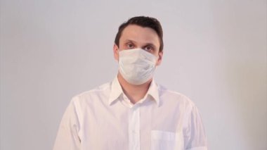 Beyaz arka planda tıbbi maske takan bir adamın portresi. Tıbbi ekipmanların tanıtımı. Adam işaret ediyor. Karantina, kendini izole etme, koronavirüsten koruma, virüs, hastalık korkusu, tedavi, ilaç