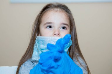 Doktor bir çift lastik eldiven giyer. Doktor ameliyata hazırlanıyor. Hastanede maskeli küçük bir kız oynuyor.