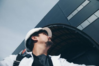 İş yerinde beyaz kasklı bir adamın portresi. Koruyucu giysiler içinde inşaat işçisi, ustabaşı. Mutlu bir işçi.