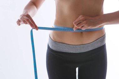 Spor egzersizlerinin sonucu: beyaz arka planda yakın plan bir mide çekimi. Kız belini bir santimetre bantla ölçüyor. Diyetin etkisi