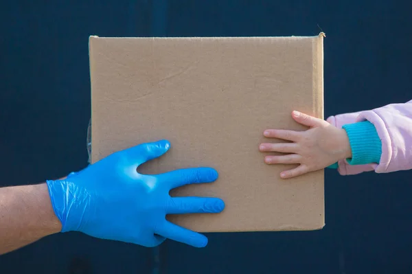 food delivery to your home. assistance to pensioners, the poor and the population. a courier in rubber gloves gives a box of food to a child. from hand to hand