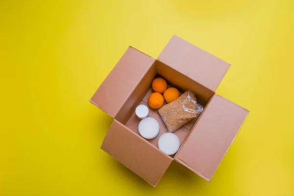 the main products for self-isolation in a box: cereals, buckwheat, fruit, canned food on a yellow background. home delivery. Assistance to population