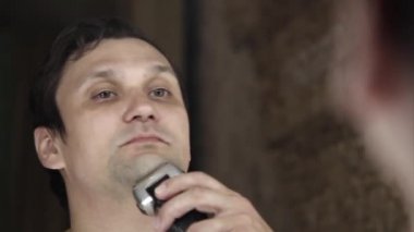 Bir adam sakalını tıraş eder. Adam sakalını elektrikli jiletle temizliyor. Sabah tedavileri banyoda. Sakal yakın plan. Boşluğu kopyala