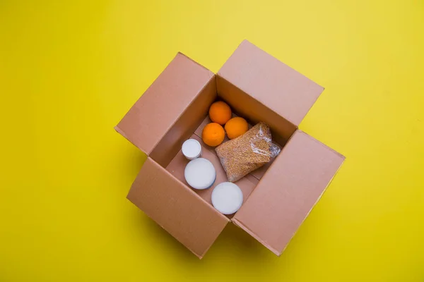 the main products for self-isolation in a box: cereals, buckwheat, fruit, canned food on a yellow background. home delivery. Assistance to population