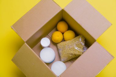 Bir kutuda kendini izole etmenin ana ürünleri: tahıllar, karabuğday, meyve, sarı arka planda konserve yiyecekler. Eve teslim. Nüfusa yardım