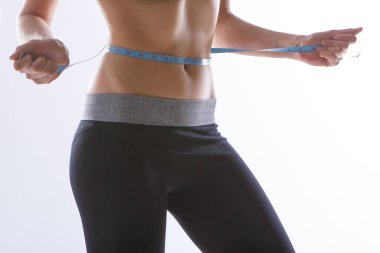 Spor egzersizlerinin sonucu: beyaz arka planda yakın plan bir mide çekimi. Kız belini bir santimetre bantla ölçüyor. Diyetin etkisi