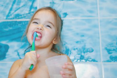 a little girl brushes her teeth and rinses her mouth in the bathroom. portrait of a child with a toothbrush clipart
