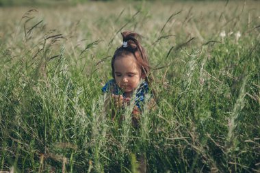 Çocuk vahşi doğanın arka planına karşı. Rus dağları, ovalar, tarlalar. Uzun otların arasındaki kız Uzağa bakar