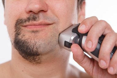 Beyaz bir arka planda izole edilmiş: bir adam sakalını tıraş eder. Adam sakalını elektrikli jiletle temizliyor. Sabah tedavileri banyoda. Sakalının yarısı yakın plan. Boşluğu kopyala