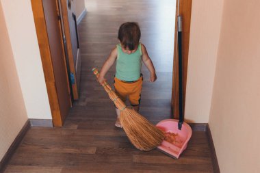 Küçük bir çocuk evi temizliyor. Kız yerleri süpürüyor. Dairede düzen sağlanıyor.