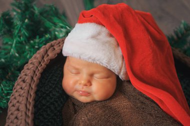Yeni doğmuş bir bebek Noel çelenginde ponponu olan kırmızı bir şapkayla uyur.
