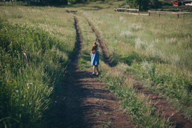 Çocuk vahşi doğanın arka planına karşı. Rus dağları, ovalar, tarlalar. Uzun otların arasındaki kız Uzağa bakar