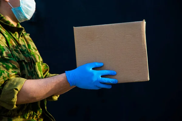 the military delivers food to your home. assistance to pensioners, the poor and the population. a courier in rubber gloves holds a box on a black background.