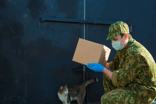 the military delivers food to your home. assistance to pensioners, the poor and the population. a courier in rubber gloves holds a box. cat at the gate. animal meets