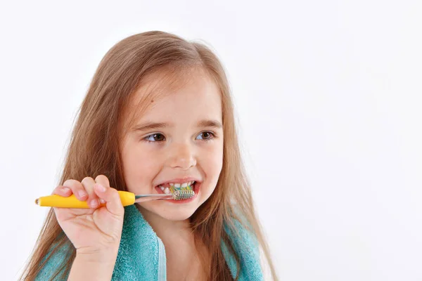 少女は白い背景に歯を磨く 黄色い歯ブラシを持つ子供の肖像画です 首の周りに青いタオル 朝の衛生手順 — ストック写真