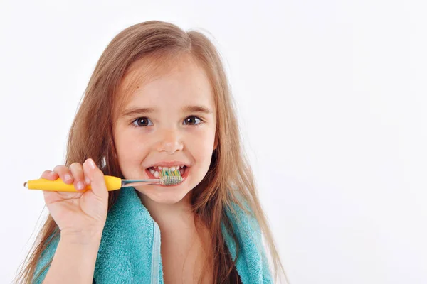 少女は白い背景に歯を磨く 黄色い歯ブラシを持つ子供の肖像画です 首の周りに青いタオル 朝の衛生手順 — ストック写真