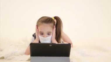 Salgın: tıbbi maskeli bir çocuğun uzaktan öğrenmesi. Hasta bir kız arkasında dizüstü bilgisayar bırakmış.