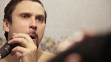 Bir adam sakalını tıraş eder. Adam sakalını elektrikli jiletle temizliyor. Sabah tedavileri banyoda. Sakalının yarısı yakın plan. Boşluğu kopyala