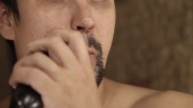 Bir adam sakalını tıraş eder. Adam sakalını elektrikli jiletle temizliyor. Sabah tedavileri banyoda. Sakalının yarısı yakın plan. Boşluğu kopyala