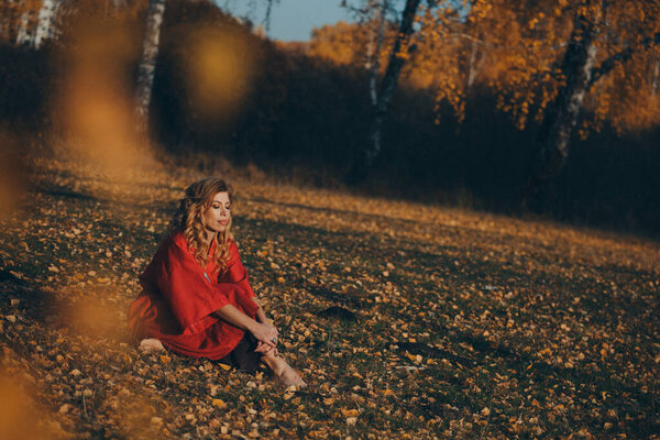 Beautiful girl in a red dress in the autumn forest. nature walk. getting energy from the sun, trees. fairitale scene of a woman laying in the forest