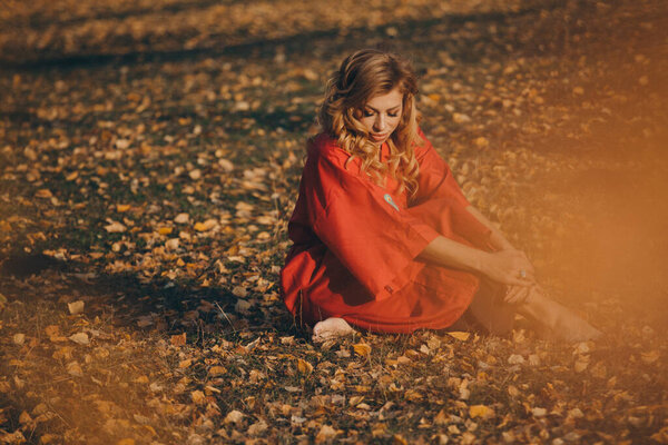 Beautiful girl in a red dress in the autumn forest. nature walk. getting energy from the sun, trees. fairitale scene of a woman laying in the forest