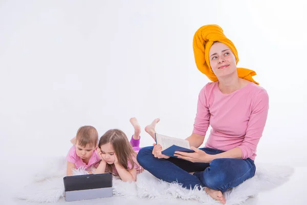 a woman reads a book, Children watch a cartoon on a tablet. mom washed her hair. towel on the head. Hobbies and recreation with gadgets. Family vacation, spend time together. home schooling.