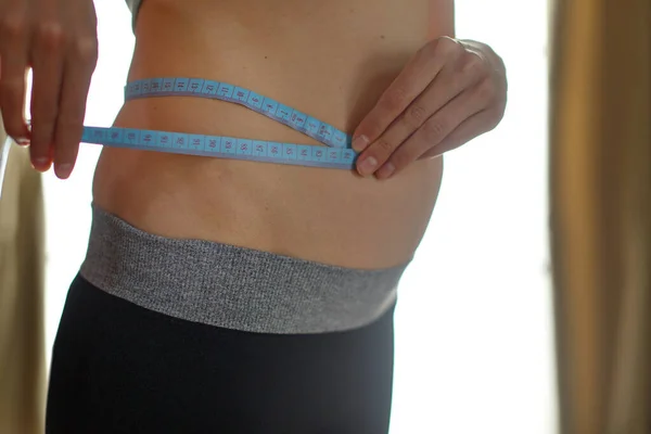 the result of sports exercises: a toned stomach close-up on a white background. The girl measures her waist with a centimeter tape. Influence of diet