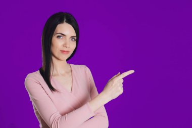Güzel bir kız parmağını gösterir. Mor arka planda bir model. kopyalama alanı. reklam afişi