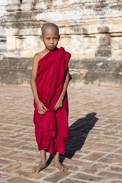 Bagan, Myanmar, 29 Aralık 2017: Genç Budist acemi standları bir pagoda Bagan, Myanmar platformu onun kırmızı elbise ile